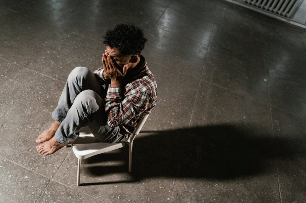 An overhead view of a man sitting alone in distress on a chair indoors, capturing anxiety and solitude.